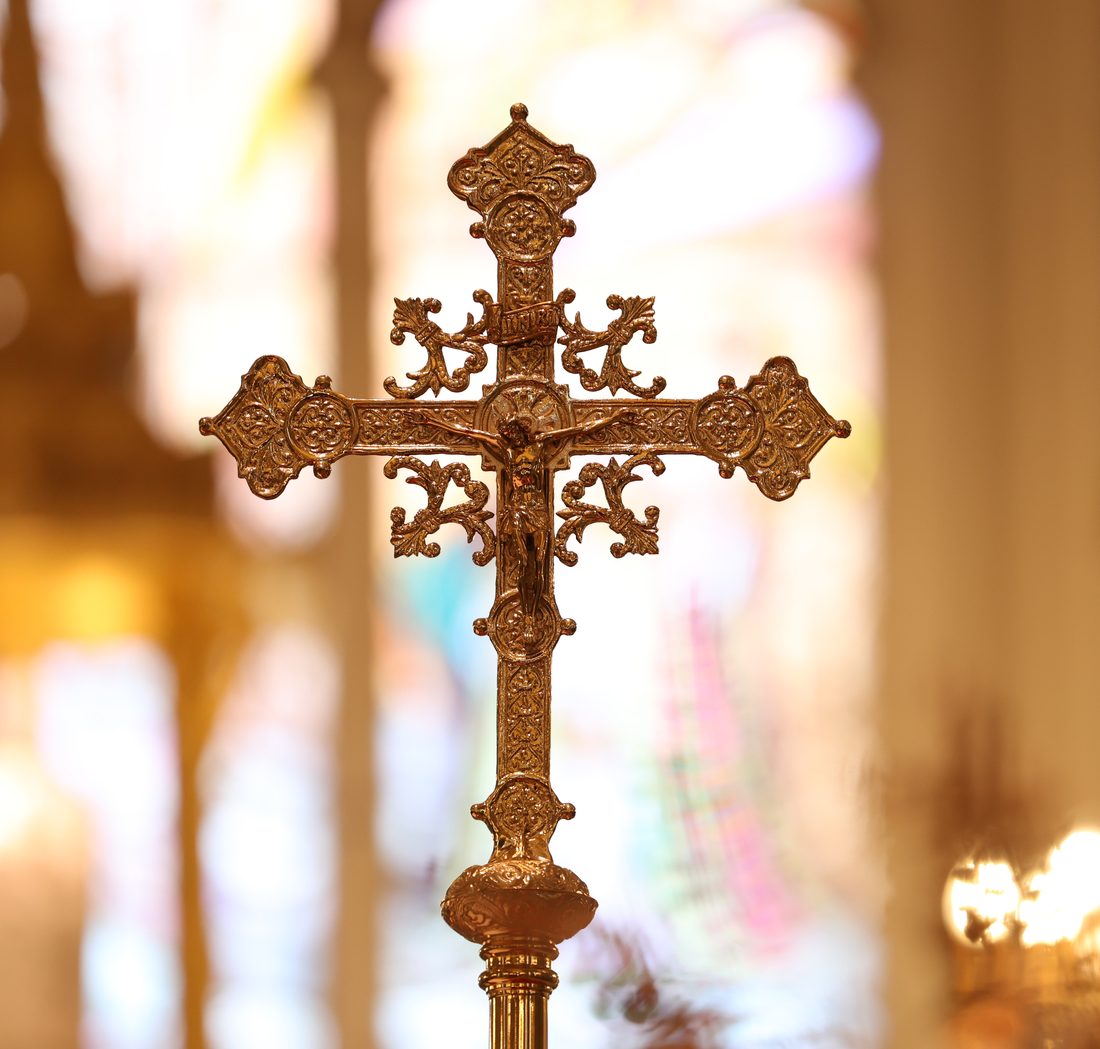 Ornate gold crucifix with church windows and candles behind it