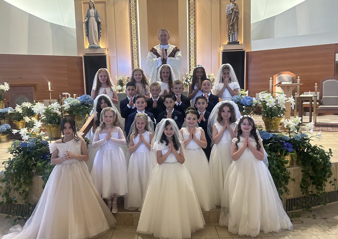 Children in First Communion attire with a priest at the altar