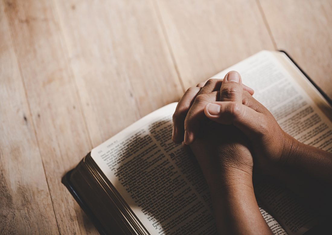 Hands folded in prayer on an open Bible