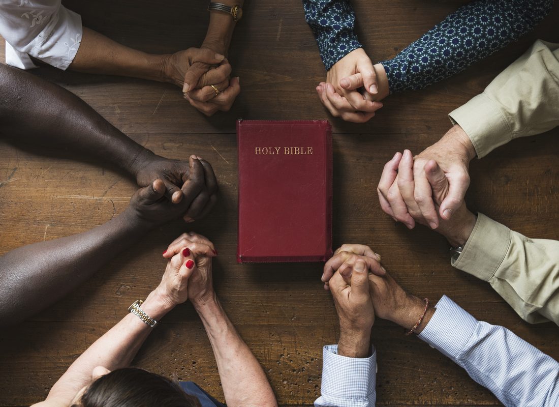 A group praying with hands folded around a Bible