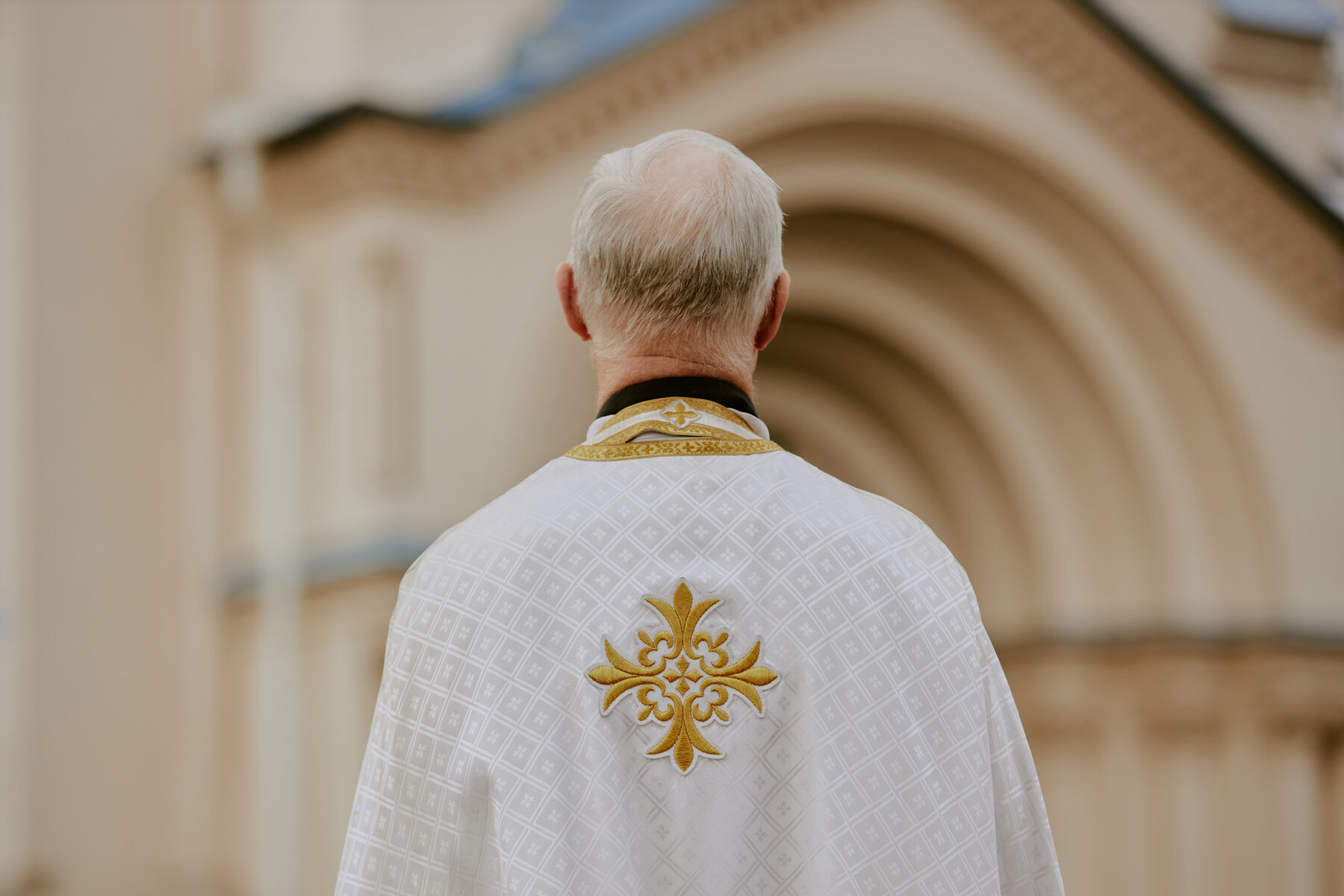 A priest in white vestments facing a church doorway