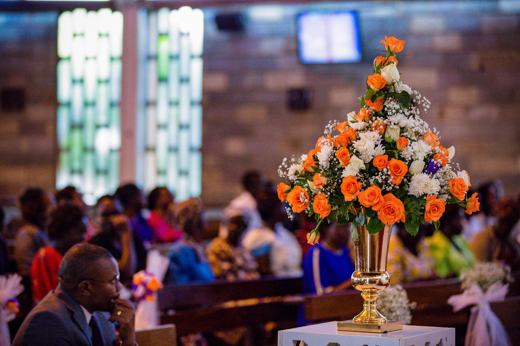 Congregation in church behind an arrangement of orange and white flowers