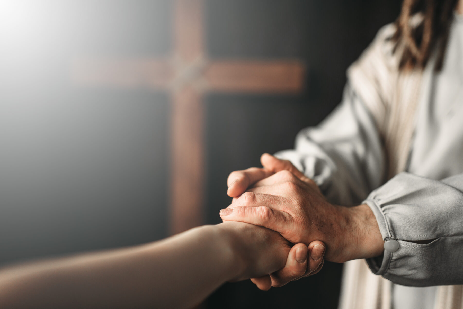 Two hands clasped in front of a cross
